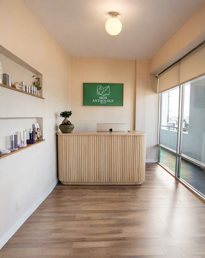 The Skin Anthology front desk with a wood slat counter, product shelves and the green Skin Anthology sign on the wall