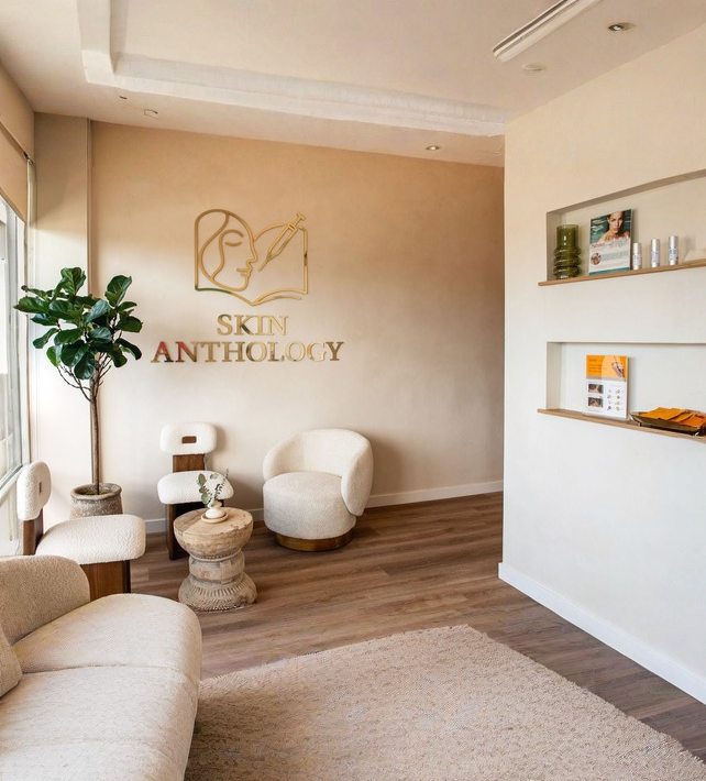 The Skin Anthology waiting room with the gold Skin Anthology logo on the wall, cream lounge chairs and a potted plant