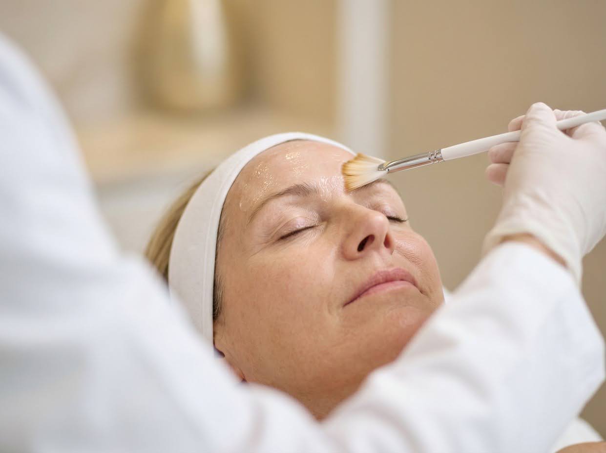 Woman lying back with eyes closed as a fan brush applies solution to her forehead