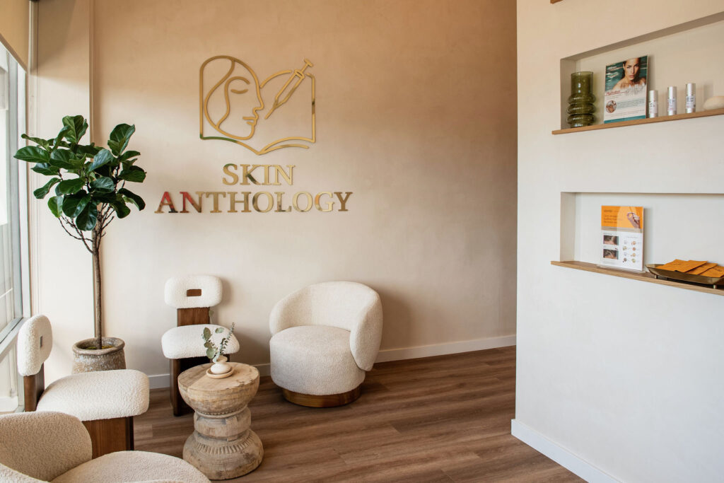 The Skin Anthology lounge with cream armchairs, a round side table and the gold Skin Anthology logo on the wall